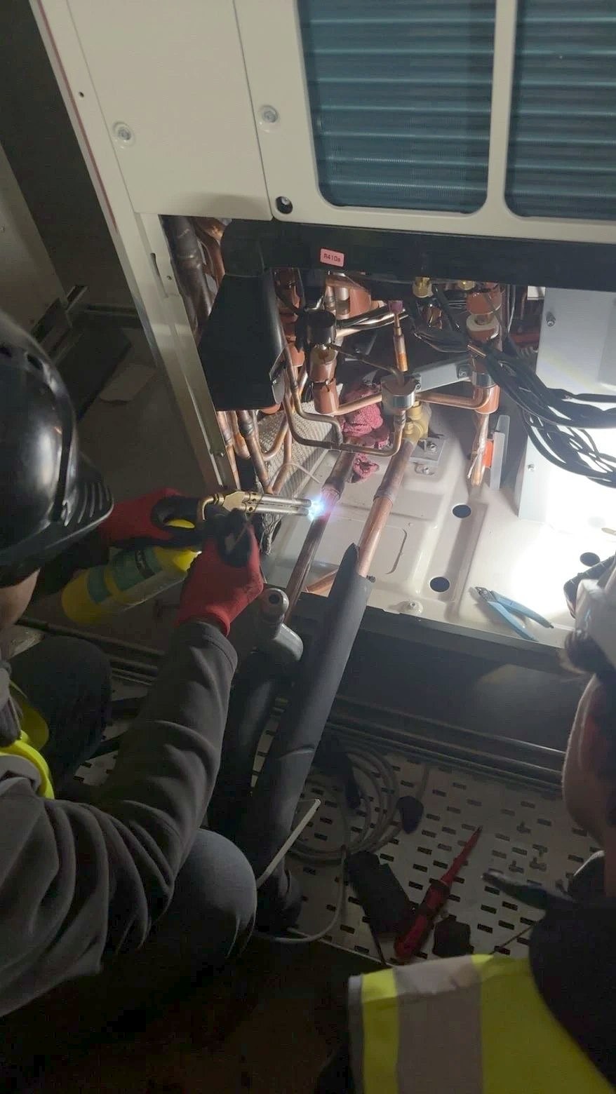 Two AV Unibrak engineers on site, one brazing copper refrigerant pipework on an air conditioning unit
